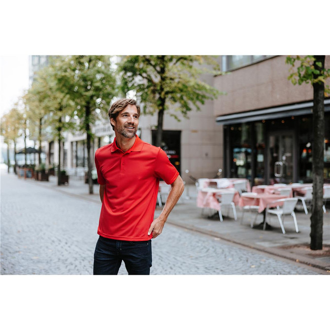 A red polo shirt worn by a man standing on a city street, surrounded by trees and outdoor seating.