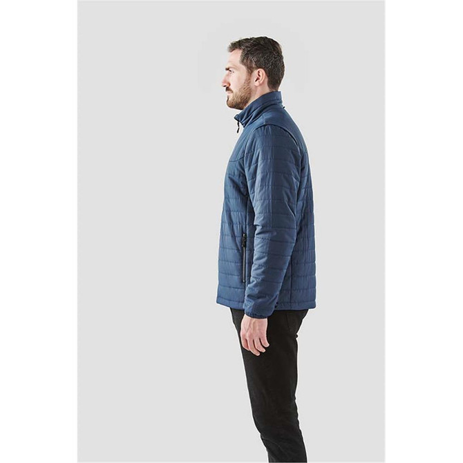 A man wearing a navy blue quilted jacket, standing in profile against a plain background. The jacket features a logo.