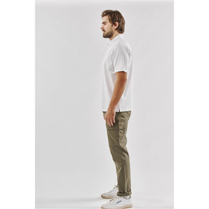 A man in a white polo shirt stands sideways, paired with olive green pants and white sneakers. The shirt has a logo.