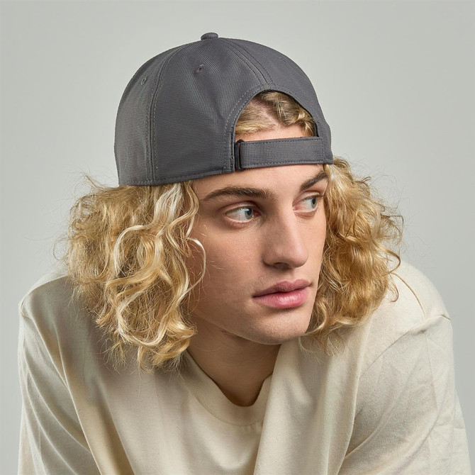 A cap made from recycled polyester in grey, worn by a model with curly blonde hair. It features a logo on the front.