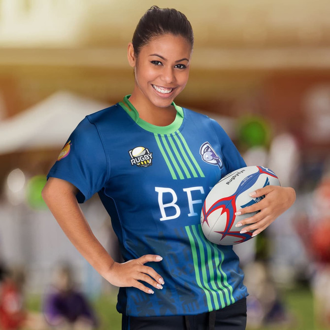 A women's rugby t-shirt in blue with green stripes, featuring a logo, paired with a rugby ball.
