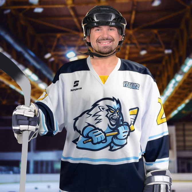 A hockey player in a white and navy custom jersey featuring a graphic design, holding a hockey stick, and wearing a helmet.