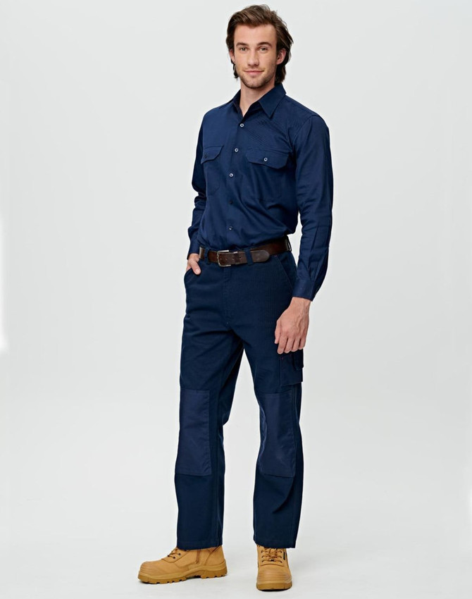 A man wearing beige work pants featuring pockets and reinforced knee patches, paired with a matching long-sleeve shirt.