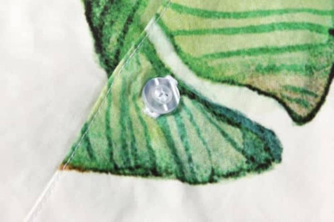A close-up of a button on a fabric featuring a green and white fish design, with a faint background.