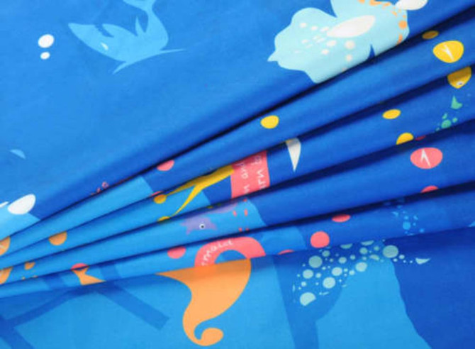 A vibrant blue beach towel featuring colourful underwater motifs and a logo. It has a double-faced pile texture.