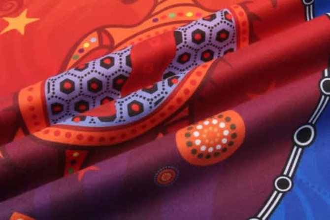 A HAND TOWEL features vibrant patterns in red, purple, and orange, with decorative motifs and a logo.