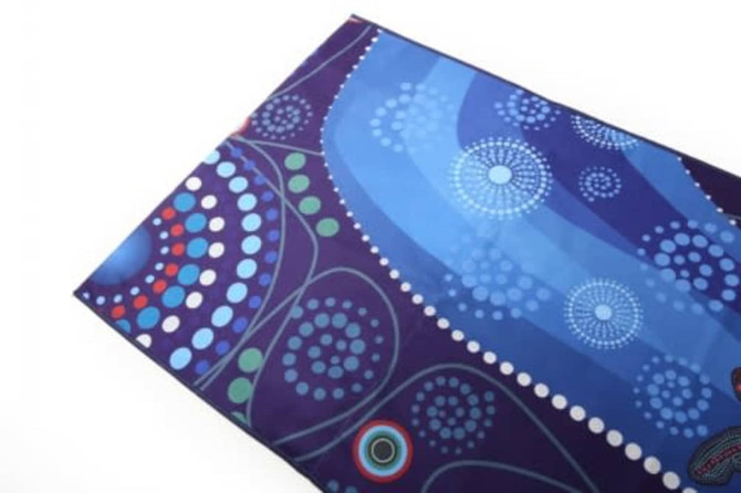 A spread towel featuring vibrant blues and purple patterns, decorated with dot motifs and swirls. It has a logo.