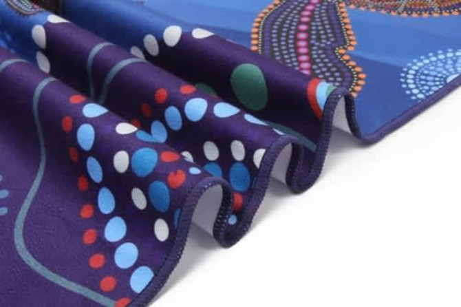 A patterned towel in blue, purple, and multicoloured dots, featuring a vibrant design and a visible logo.