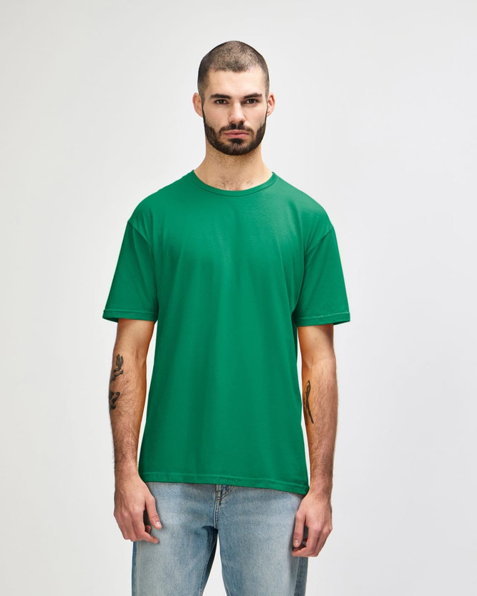 A man wearing a green Gildan Softstyle adult t-shirt, standing against a plain background, paired with blue jeans.