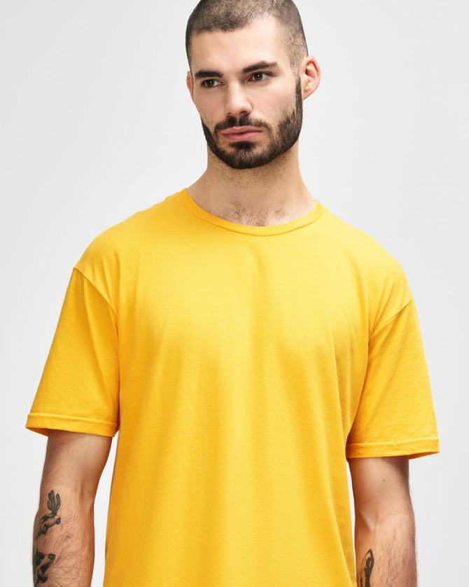 A smiling young man wearing a vibrant yellow Gildan Softstyle adult t-shirt with a logo on it.