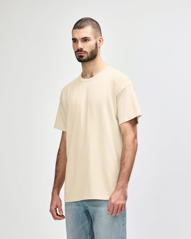 A beige Gildan Softstyle adult T-shirt features a relaxed fit and short sleeves, paired with light blue jeans.