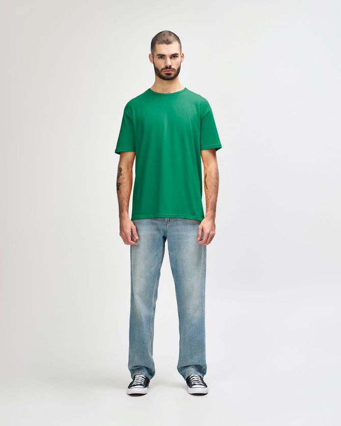 A green Gildan Softstyle adult t-shirt displayed on a male model, paired with light blue jeans.