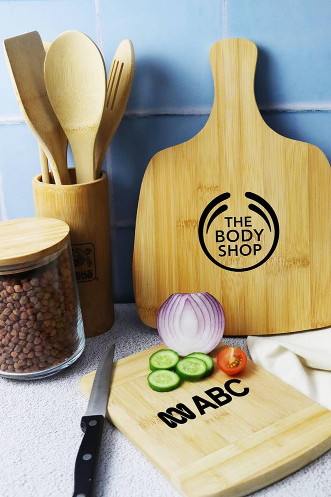 A bamboo cutting board with a handle, surrounded by kitchen utensils, sliced vegetables, and a glass container.