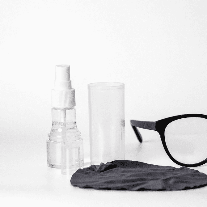 An eye glass cleaner set featuring a spray bottle, a clear container, a black cleaning cloth, and a pair of black glasses.
