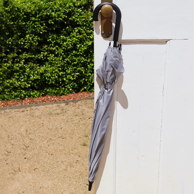 A grey umbrella hanging on a door handle, featuring a curved black handle.