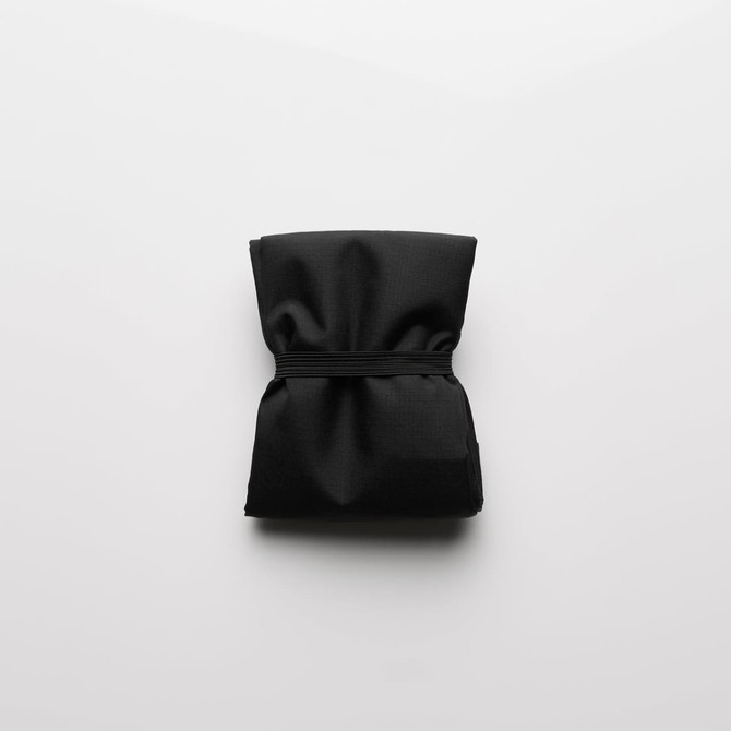 A folded black reusable grocery bag secured with an elastic band, featuring subtle texture and a minimal design.