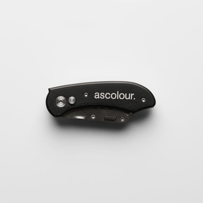 A black ASC Utility Knife with a sleek design, featuring a foldable blade and a logo on the surface.