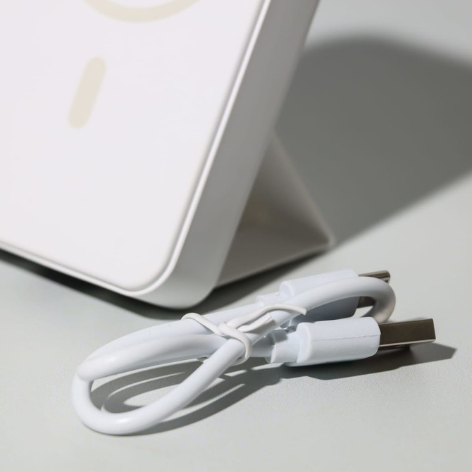 A white wireless charging power bank with a USB cable beside it, featuring a sleek, modern design.