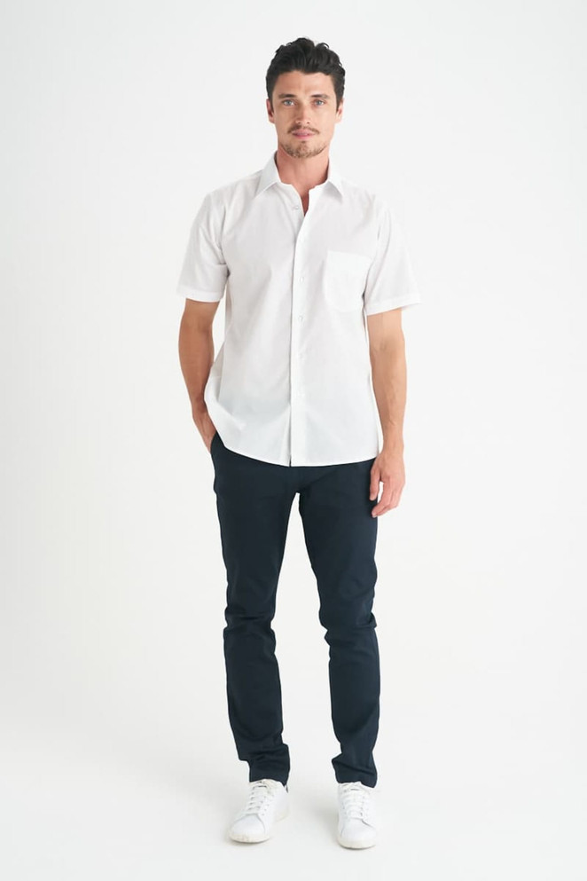A man wearing a white short sleeve button-up shirt with a chest pocket, paired with dark trousers and white shoes.
