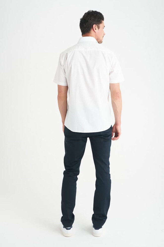 A man wearing a white short sleeve button-up shirt, standing with his back to the camera, paired with dark jeans.