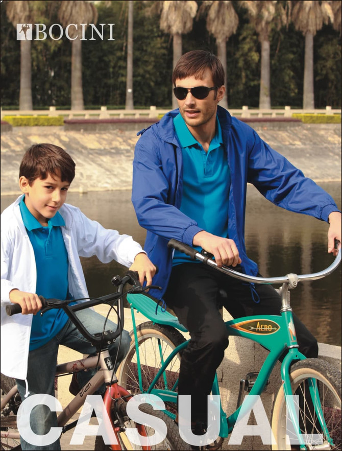 A blue kids' yachtman's jacket with lining displayed on a child and an adult, both on bicycles near a water body.