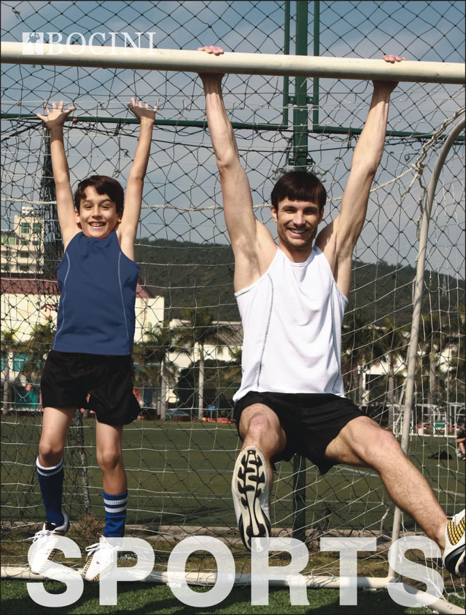 A white singlet shirt is worn by an adult and a child, both hanging from a soccer goal. The scene is outdoors with a sunny backdrop.