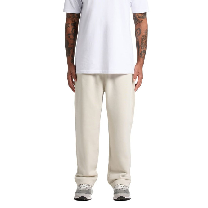 A person stands in relaxed cream track pants paired with a white t-shirt. The pants have a logo detail.