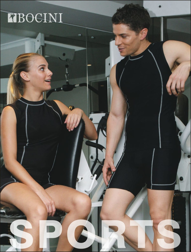 Two models in black athletic performance wear, featuring contrasting piping, discussing in a gym setting.