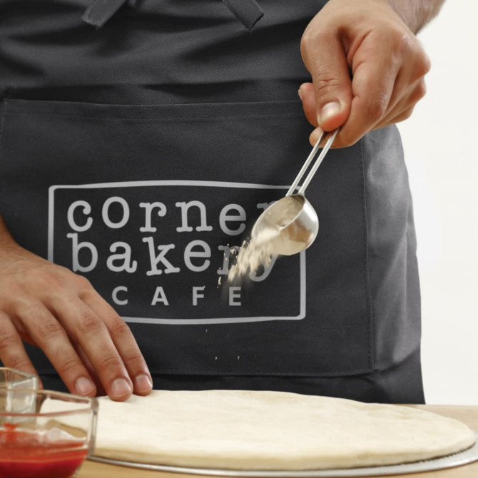 A dark grey waist apron features a logo, with a person using a scoop above a pizza dough.