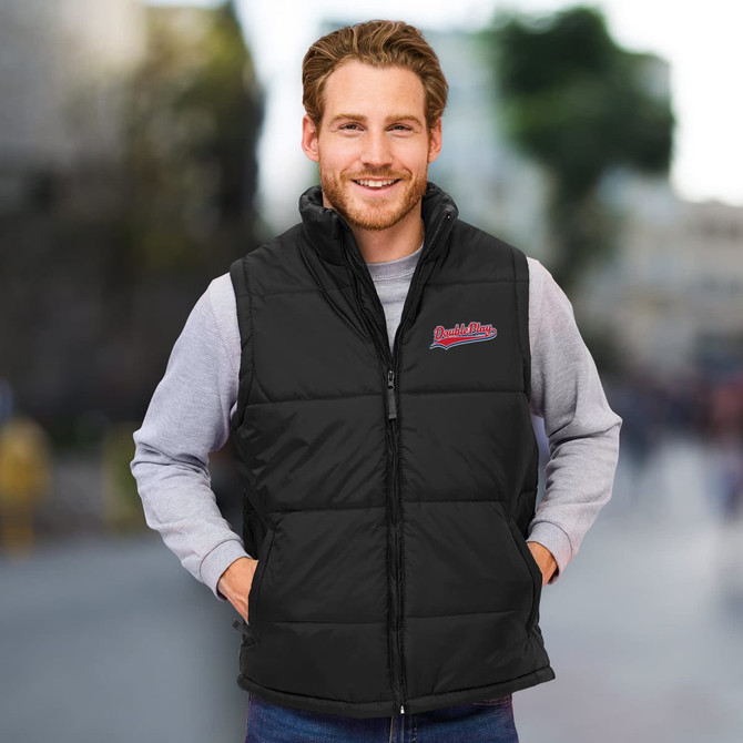 A unisex black puffer vest with a high collar and a logo on the chest. The model is smiling outdoors.