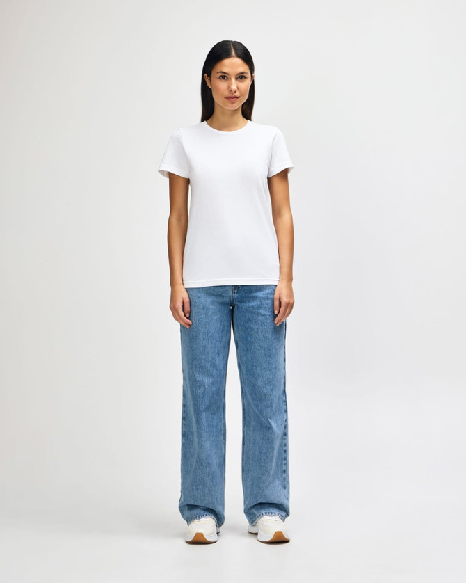A model wearing a white ladies midweight T-shirt paired with blue jeans and white sneakers, standing in a neutral background.