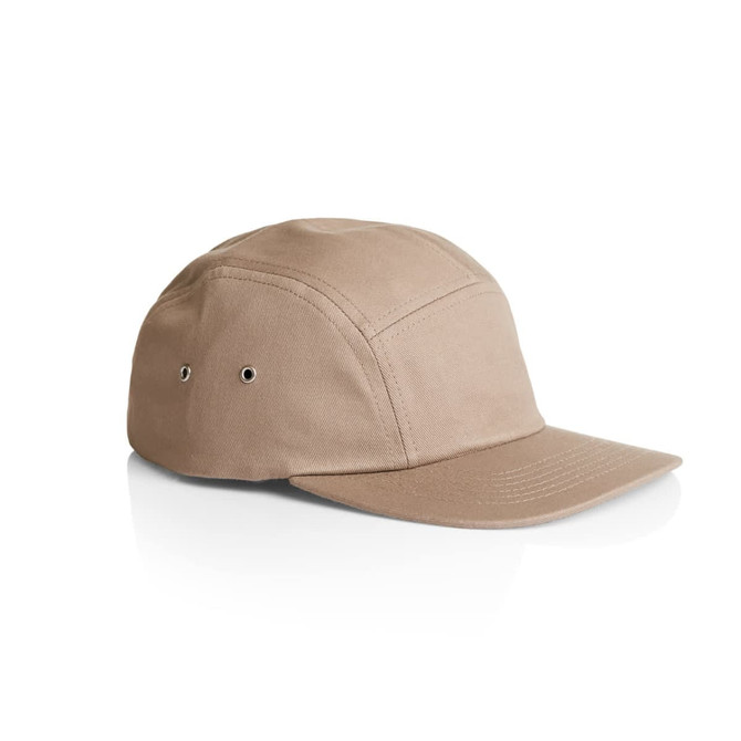 A tan five-panel cap featuring eyelets for ventilation and a curved brim, with a logo on the side.