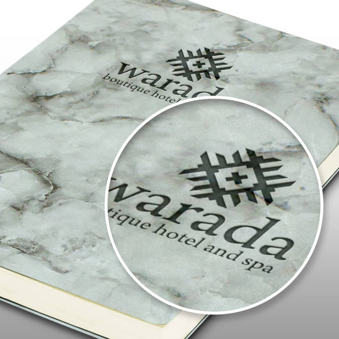 A marble-patterned soft cover notebook in shades of grey, featuring a logo on the front.