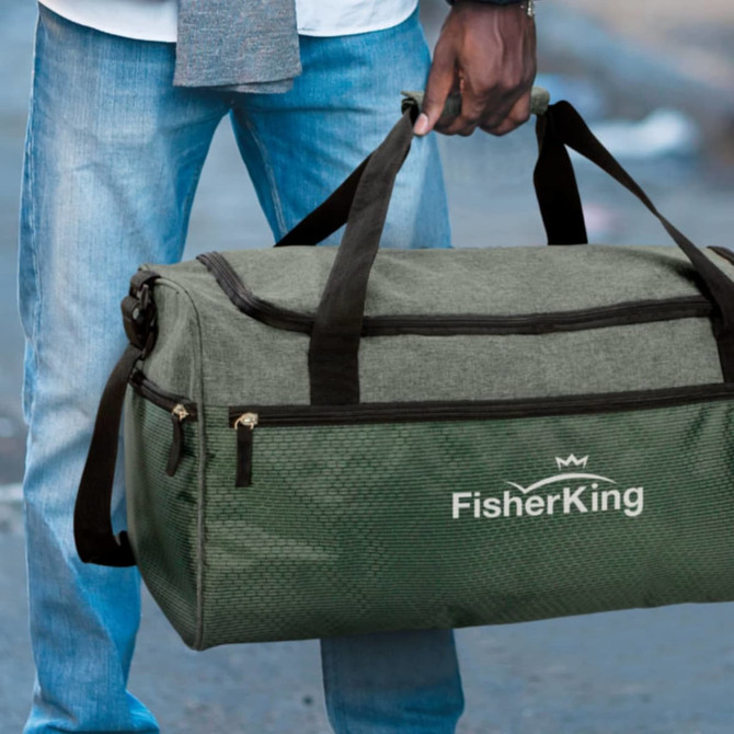 A green duffle bag with handles and a logo, held by a person standing outdoors in casual attire.