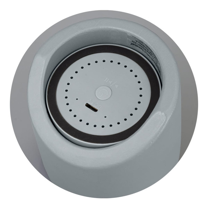 A Bluetooth mini speaker in light grey with a circular base and a small charging port at the bottom.