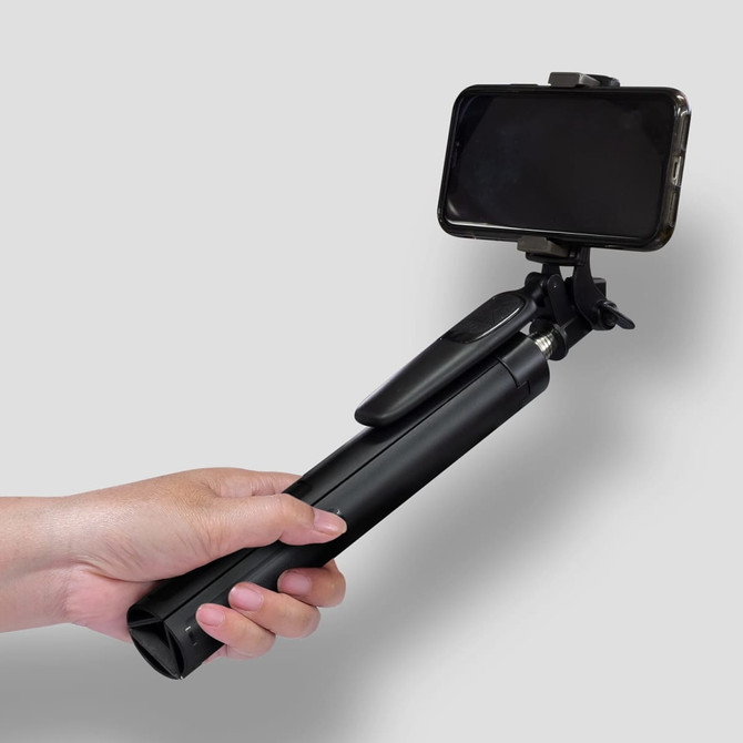 A black selfie stick tripod held in a hand, featuring a phone holder at the top.