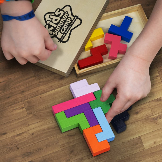 A colourful wooden pentomino puzzle set displayed on a wooden surface, with hands assembling the pieces.