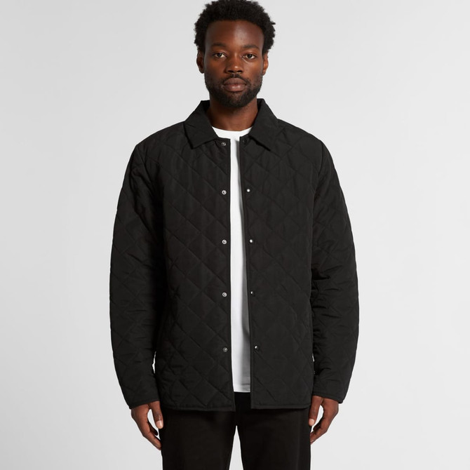 A man wearing a black quilted jacket with a button-up front and a collared neck. The jacket has a logo.