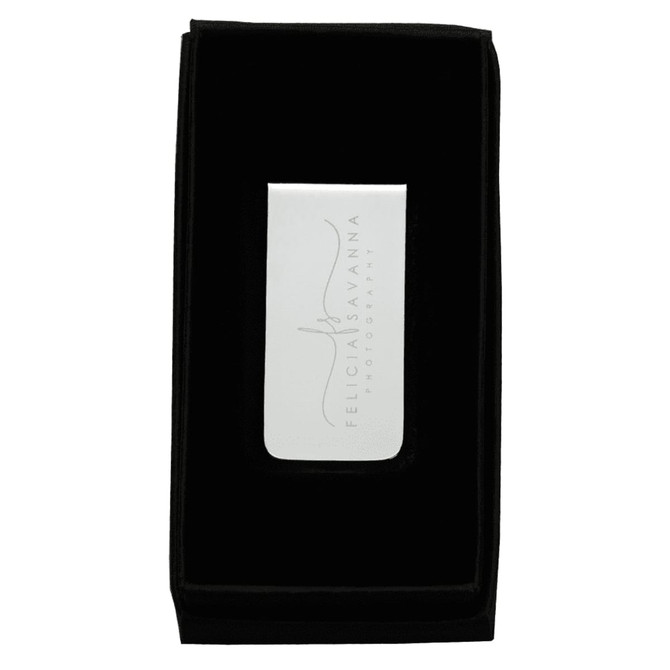 A sleek metal money clip in a black velvet presentation box, with a reflective surface and a subtle logo.