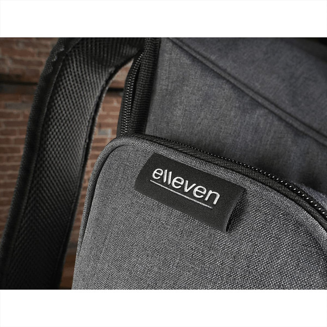 A grey backpack with a textured fabric and a logo patch. It features a zippered pocket and padded straps.