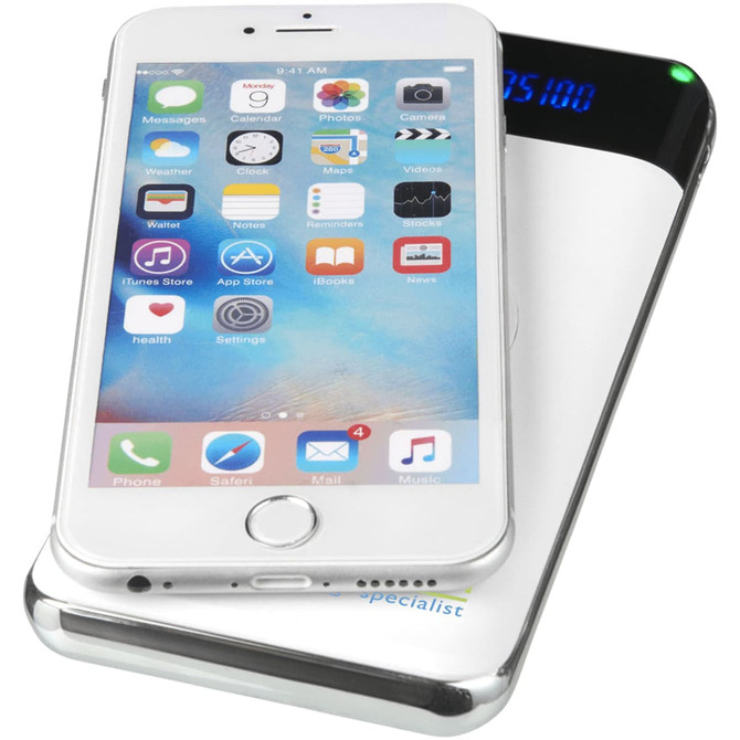 A silver wireless power bank with a digital display, topped with a smartphone displaying various apps.