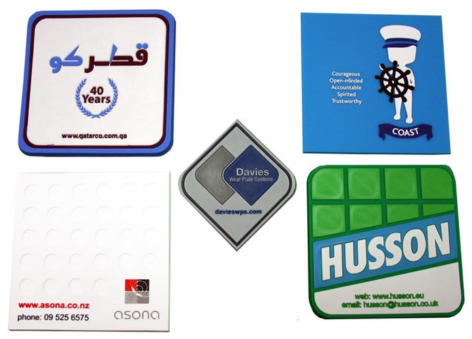 A selection of custom PVC coasters in various shapes and colours, featuring logos and designs.