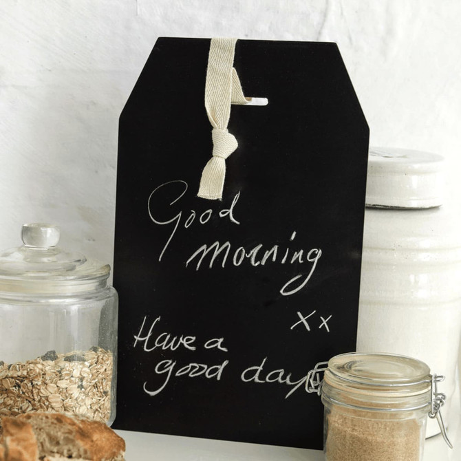 A black chalkboard sign with a tag shape, featuring handwritten messages and a hanging ribbon.