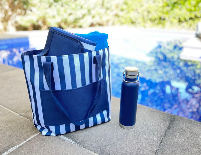 A navy and white striped tote bag with a drink bottle and additional items inside, placed beside a pool.