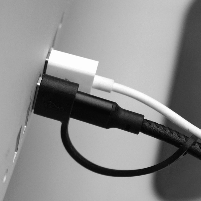 A black and white image of a black and white charging cable plugged into a device. Features a logo on the cable.