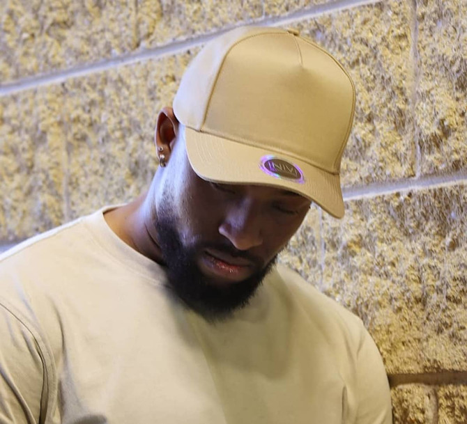 A beige cap is displayed on a model with a neutral background, featuring a branding logo.