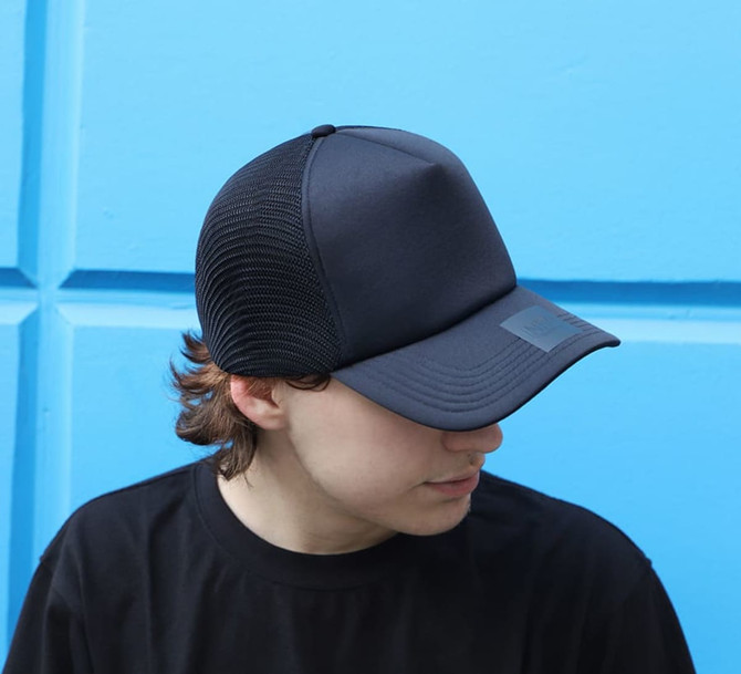 A black trucker cap made of polyester and mesh, featuring a solid front and mesh sides, resting on a blue background.