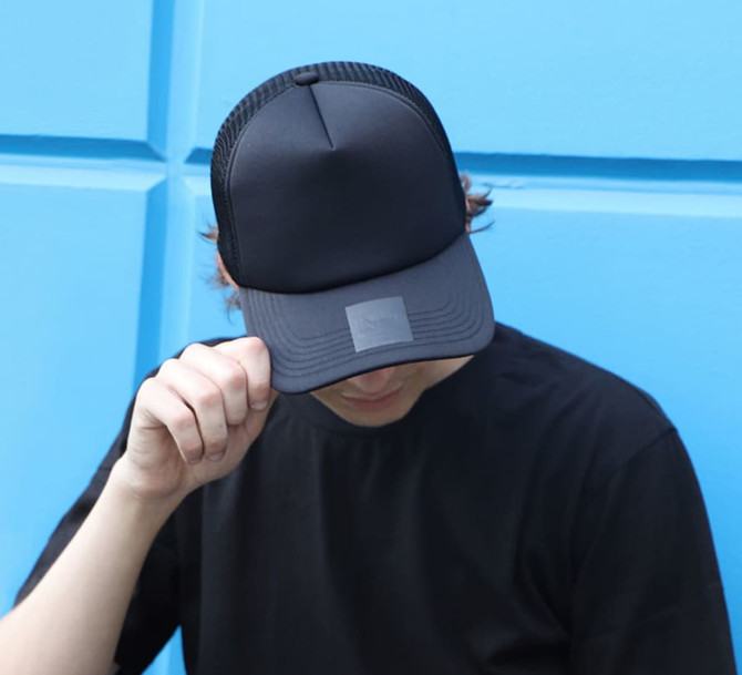 A black trucker cap with a mesh back, featuring a logo, worn by a person against a blue background.