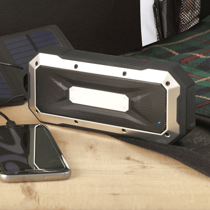 A waterproof outdoor Bluetooth speaker in black and silver, placed next to a smartphone on a wooden surface.