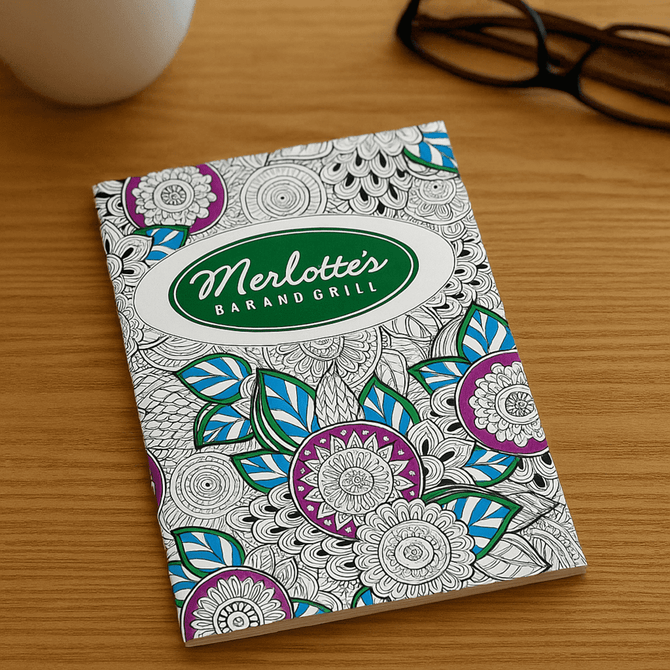 An A4 colouring book with intricate floral designs in purple, blue, and green on a white cover, featuring a logo.